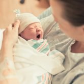 Newborn baby wrapped in a blanket being gently held by a midwife
